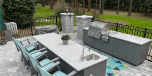 Full view of an outdoor kitchen with a grill, a sink, cabinets, and chairs.